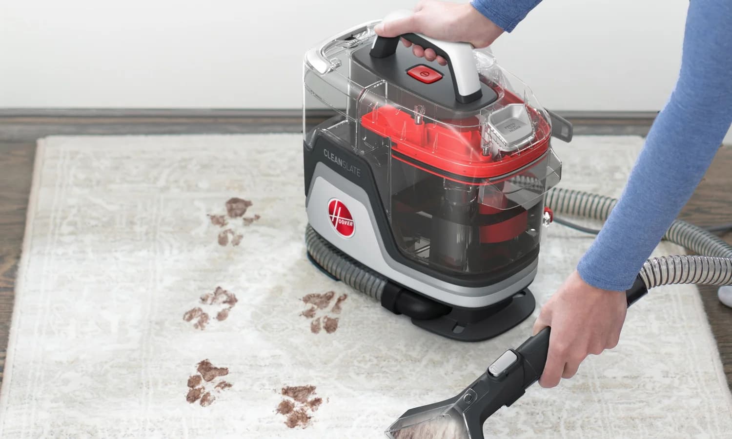 Person using a Hoover CleanSlate hand tool beside a soiled household rug