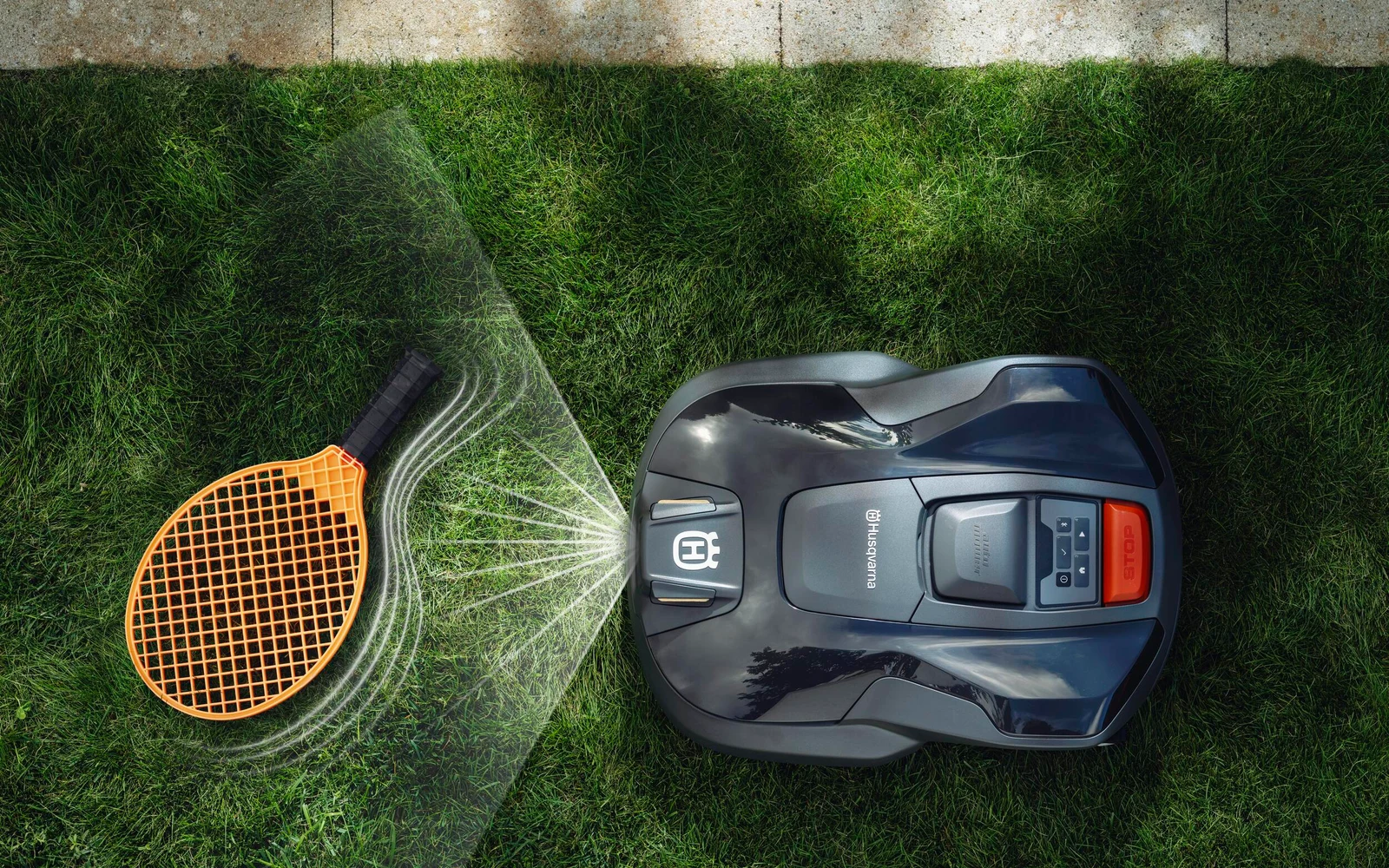 Husqvarna Automower robotic lawn mower operating beside a tennis racket on grass