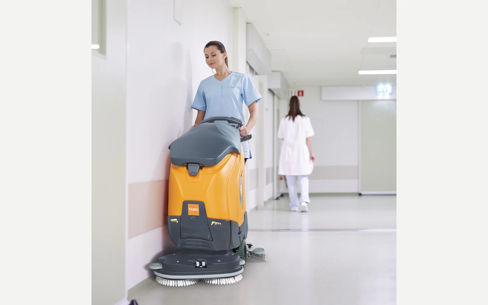 Operator using a TASKI ULTIMAXX walk-behind floor scrubber in a healthcare corridor